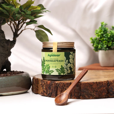 Apidear MoringaPrash jar surrounded by fresh moringa leaves, seeds, and herbal ingredients showing natural formulation